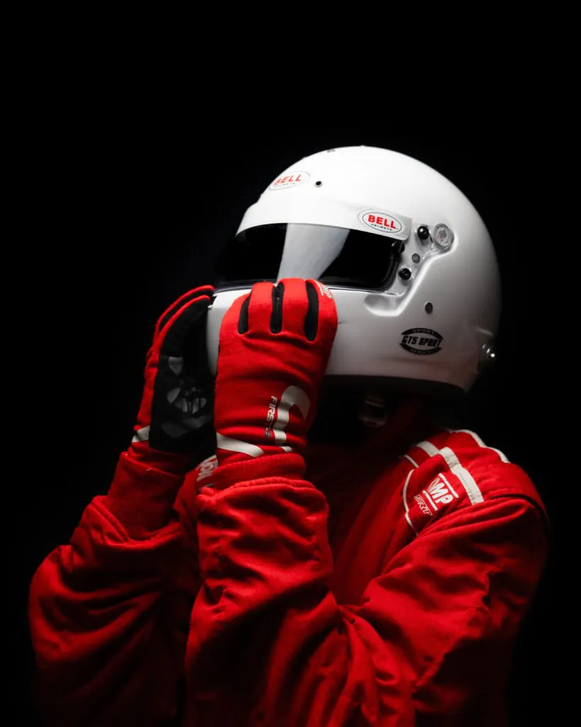 Piloto con mono rojo ajustándose el casco blanco sobre fondo negro