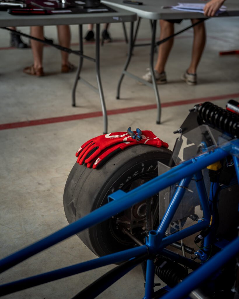 Guantes rojos apoyados en la rueda junto al chasis tubular azul