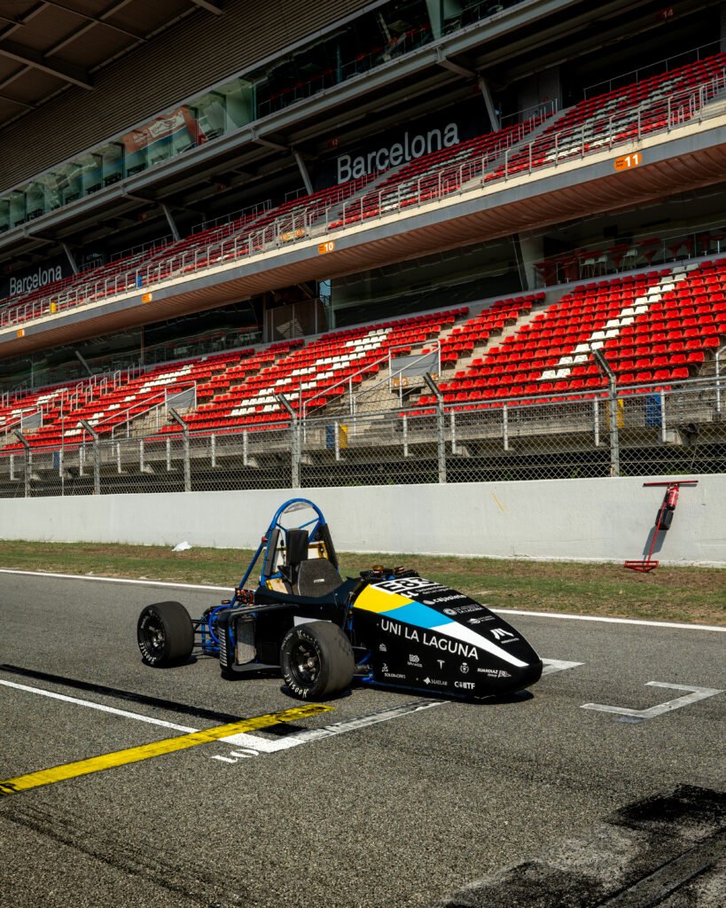 Monoplaza en pista con la tribuna principal del circuito al fondo