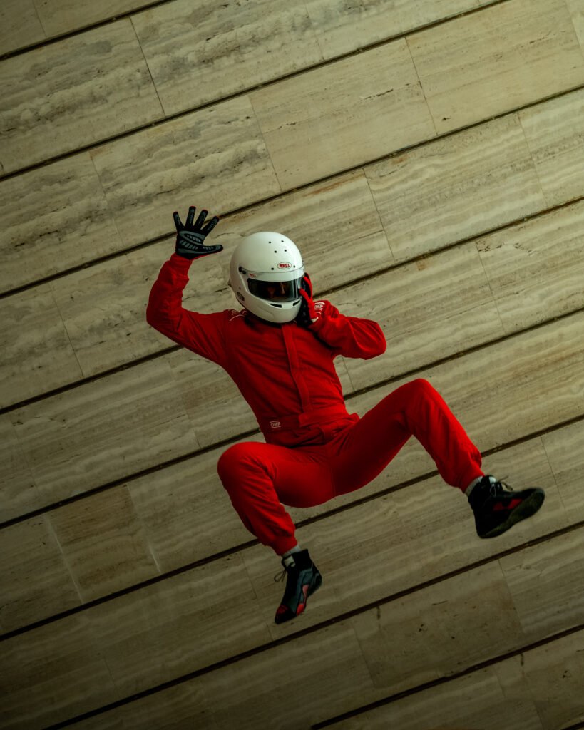 Piloto con mono rojo y casco saltando junto a un muro de hormigón